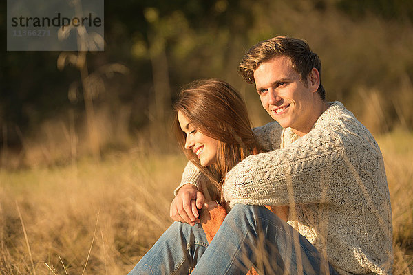 Junges Paar sitzt in ländlicher Umgebung und lächelt