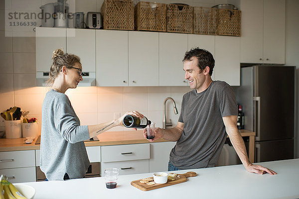 Mittleres erwachsenes Paar gießt Rotwein in die Küche