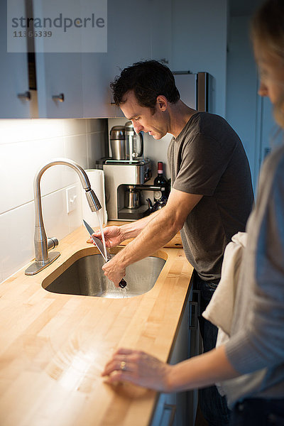 Mittleres erwachsenes Paar beim Waschen des Küchenmessers am Spülbecken