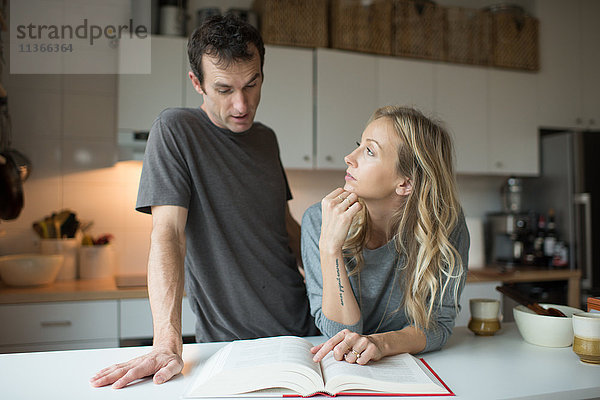 Mittleres erwachsenes Paar liest Rezeptbuch in der Küche