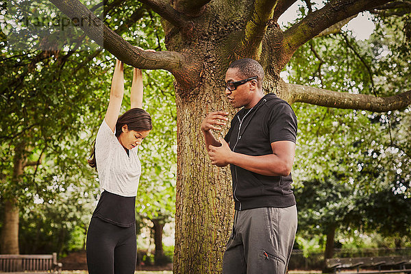 Personal Trainerin  die die Frau mit Hilfe eines Parkbaumzweiges in Pull-Ups unterweist.