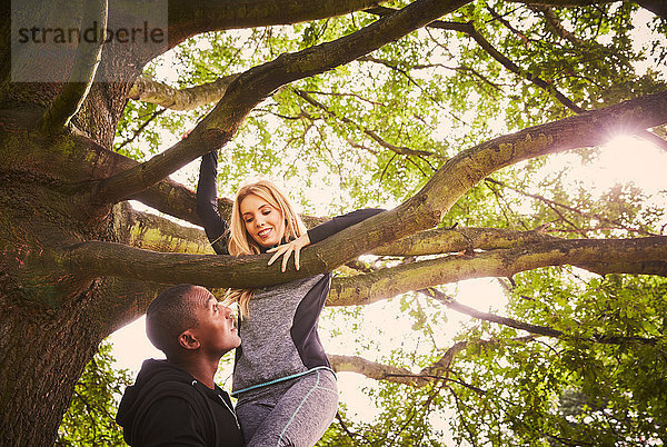 Personal Trainerin hebt junge Frau zum Klettern auf den Parkbaum