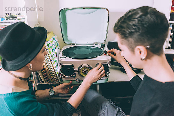 Über-Schulter-Ansicht von zwei jungen Frauen  die Vinyl auf einem Vintage-Plattenspieler spielen