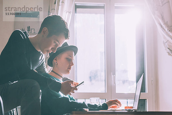 Zwei junge Freundinnen mit Smartphone und Laptop im Wohnzimmer