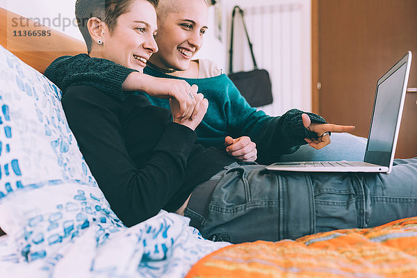 Junges lesbisches Paar  das auf dem Bett liegt und auf einen Laptop zeigt