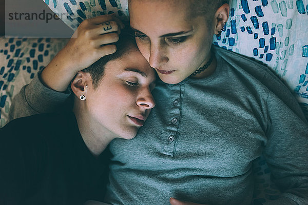 Draufsicht auf ein junges lesbisches Paar  das auf einem Bett liegt