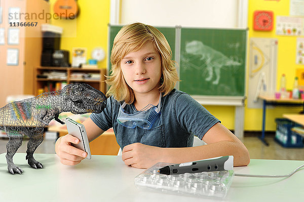 Porträt eines Jungen mit Handcomputer und 3D-Modell des Tyrannosaurus rex