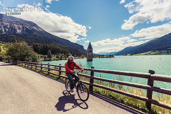 Ältere Frau radelt am See mit Curon-Glockenturm  Vinschgau  Südtirol  Italien