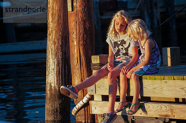 Mädchen sitzen Seite an Seite auf dem Pier