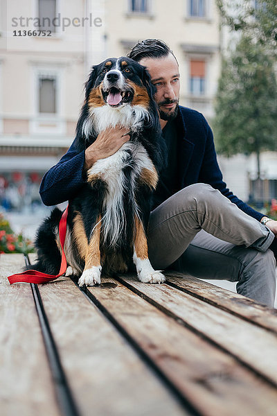 Mittelgroßer erwachsener Mann sitzt mit Haushund auf einer Bank auf dem Stadtplatz