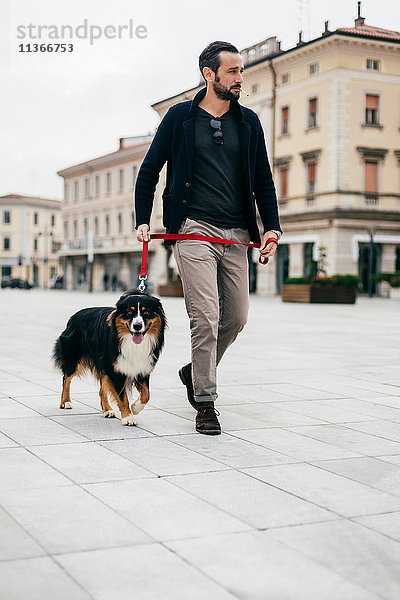 Mittelgroßer erwachsener Mann geht mit Hund auf dem Stadtplatz spazieren