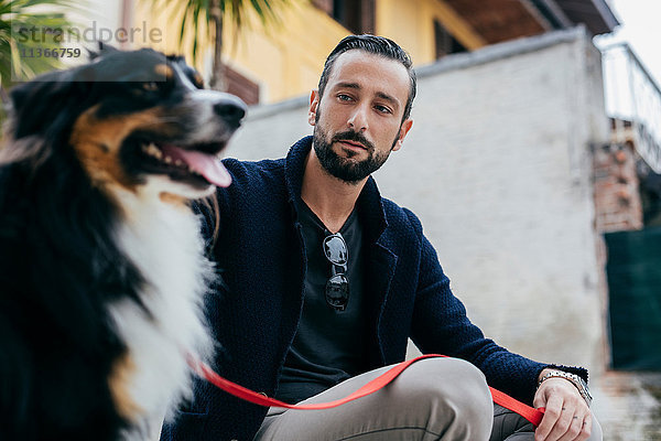 Mittelgroßer erwachsener Mann sitzt mit Hund auf der Stadtstufe