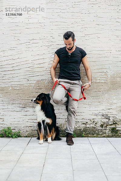 Mittelgroßer erwachsener Mann mit an die Wand gelehntem Hund