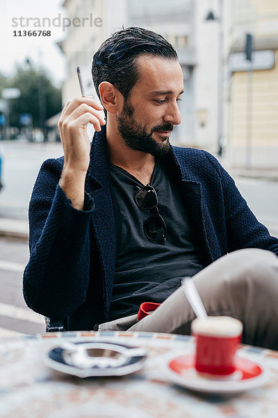 Mittelgroßer erwachsener Mann raucht Zigarette im Straßencafé