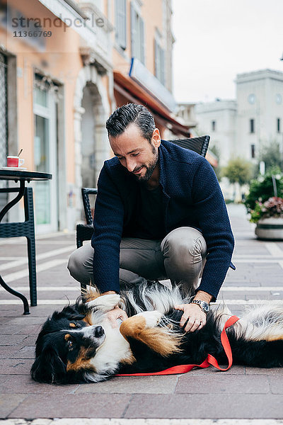 Mittelgroßer erwachsener Mann  der auf dem Stadtplatz kauert  um seinen Hund zu streicheln