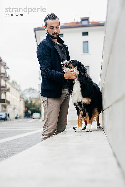 Mittelgroßer Mann streichelt Hund an der Wand in der Stadt