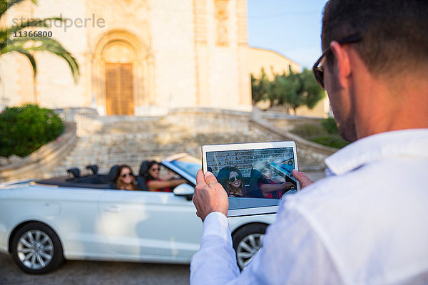 Über-Schulter-Ansicht eines Mannes  der zwei junge Touristinnen im Cabriolet fotografiert  Calvia  Mallorca  Spanien