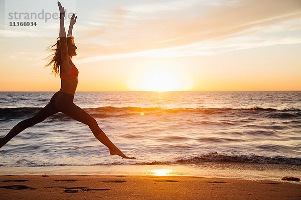 Frau springt bei Sonnenaufgang am Strand in die Luft