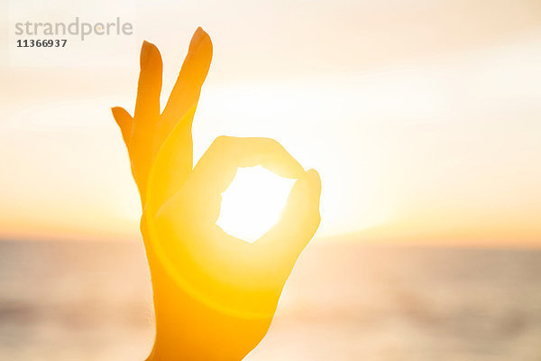 Frau umkreist bei Sonnenaufgang die Sonne mit den Fingern