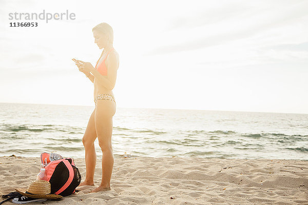 Frau am Strand schaut auf Smartphone