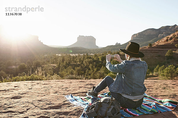 Frau sitzt auf einer Decke in der Wüste und fotografiert mit einem Smartphone  Sedona  Arizona  USA