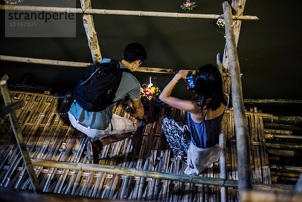 Junger Mann und Frau am Ping-Fluss in Chiang Mai während des Loy Krathong Laternenfestivals  bei dem eine schwimmende Laterne den Ping-Fluss hinuntergelassen wird  Chiang Mai  Thailand