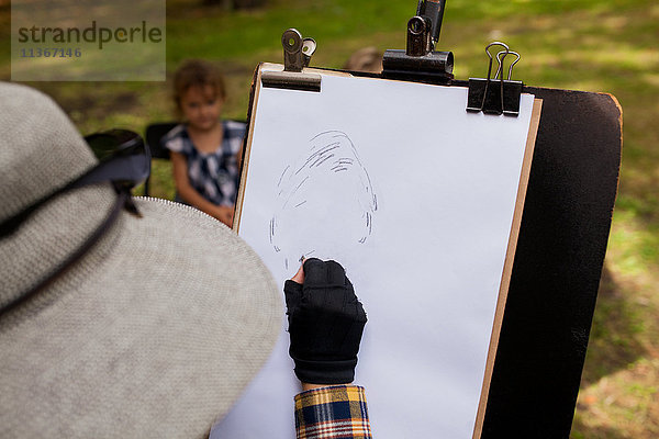 Frau skizziert Porträt eines kleinen Mädchens im Hintergrund