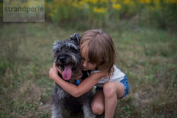 Kleines Mädchen umarmt Haushund auf Grasfeld