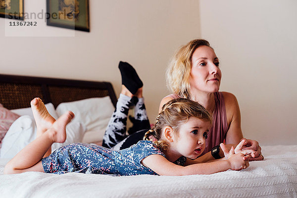 Frau liegt im Bett mit Kleinkind-Tochter vor dem Fernseher