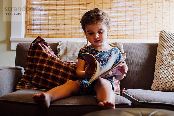 Weibliches Kleinkind sitzt auf Sofa und liest Märchenbuch