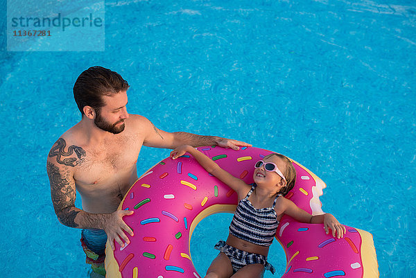 Junges Mädchen im Schwimmbad  entspannt auf aufblasbarem Ring  Vater steht neben ihr