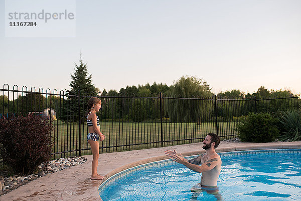 Junges Mädchen steht am Rand eines Swimmingpools  der Vater im Pool ermutigt sie  hineinzuspringen