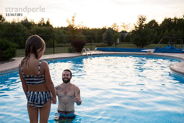 Junges Mädchen steht am Rand eines Swimmingpools  der Vater im Pool ermutigt sie  hineinzuspringen