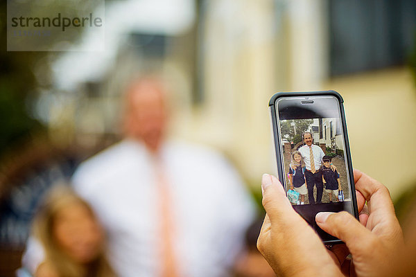 Hände der Mutter  die männliche und weibliche Grundschulzwillinge mit dem Vater auf einem Smartphone fotografiert