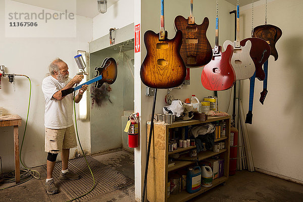 Gitarrenbauer in der Werkstatt mit Spritzpistole zum Lackieren der Gitarre