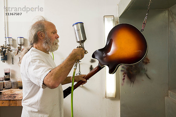 Gitarrenbauer in der Werkstatt mit Spritzpistole zum Lackieren der Gitarre
