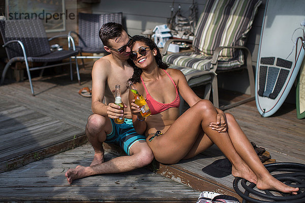 Junges Paar in Bikini und Badeshorts mit Bierflaschen auf der Veranda  Rockaway Beach  Bundesstaat New York  USA