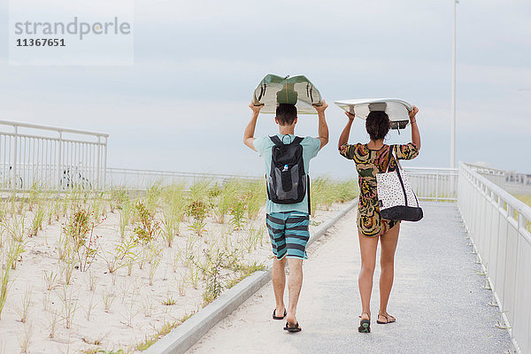 Rückansicht eines jungen Paares  das Surfbretter auf dem Kopf trägt  Rockaway Beach  New York State  USA