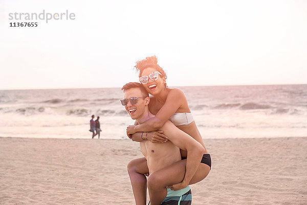 Junger Mann gibt seiner Freundin am Rockaway Beach ein Schweinchen zurück  New York State  USA