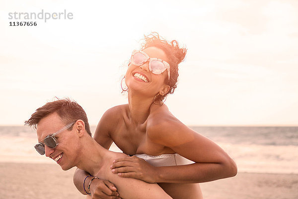 Junger Mann gibt seiner Freundin am Rockaway Beach ein Schweinchen zurück  New York State  USA