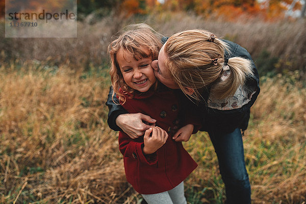 Mittlere erwachsene Frau küsst Tochter auf dem Feld auf die Wange