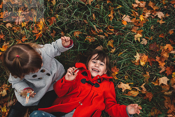 Portrait eines Mädchens und einer kleinen Schwester  die auf Gras und Herbstlaub liegen