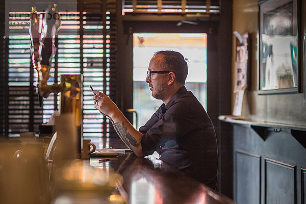 Barkeeper liest Smartphone-Texte am Tresen einer Gaststätte