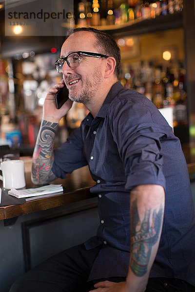 Barmann spricht mit Smartphone am Tresen einer Gaststätte