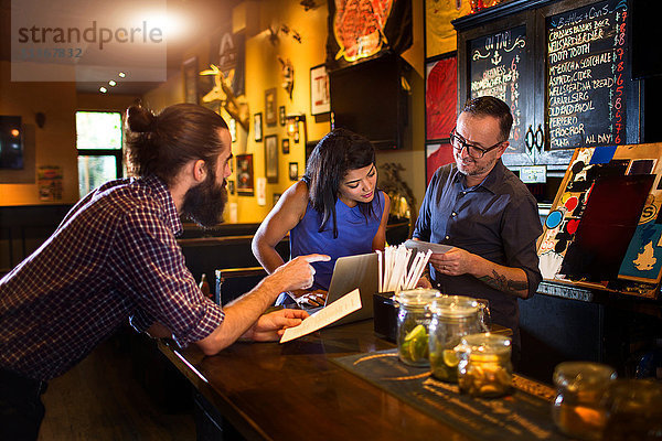 Barkeeper liest Speisekarte mit jungem Ehepaar am Tresen