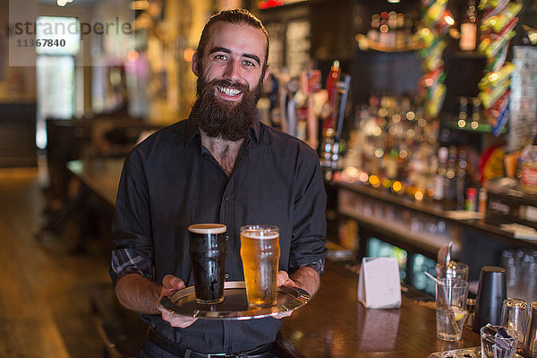 Porträt eines jungen männlichen Barkeepers mit einem Tablett mit Bier in einer Gaststätte