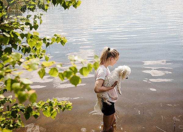 Frau steht im See und trägt einen Hund mit Coton de Tulear  Orivesi  Finnland