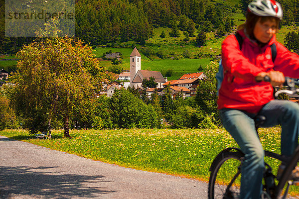 Ältere Frau radelt entlang des Dorfwegs im Vinschgau  Südtirol  Italien