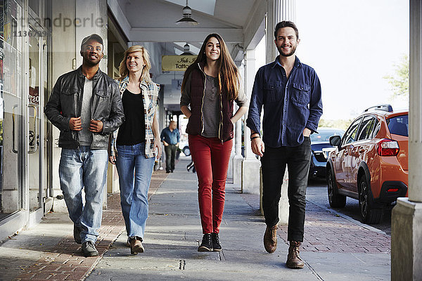 Zwei junge Männer und zwei junge Frauen gehen über einen Bürgersteig und lächeln in Schrot.