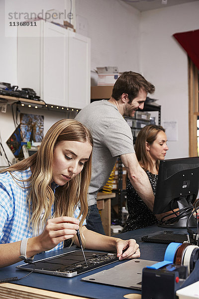 Ein Mann steht hinter zwei Frauen  die in einem Technologielabor an Schaltkreisen arbeiten.